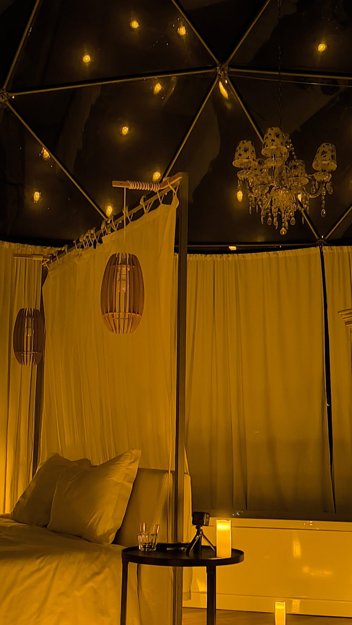 Candlelit dome interior at dusk with private bathtub and chandelier at Glamping Skies